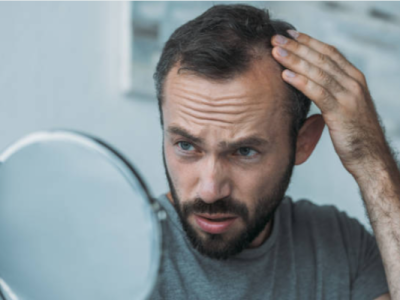 man touching his hair and looking into mirror surprised to see signs of hair loss