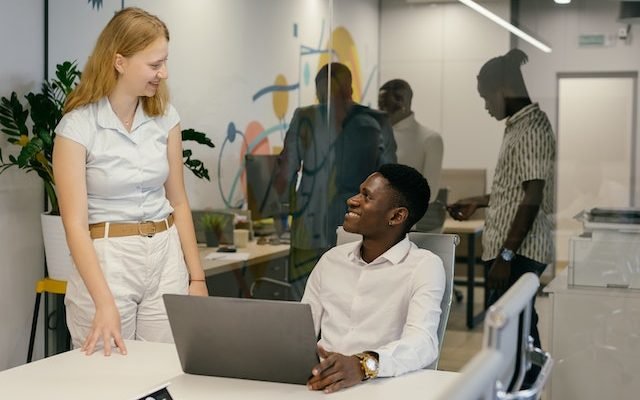 man with influence in his team sitting and talking to a female co-worker who is standing