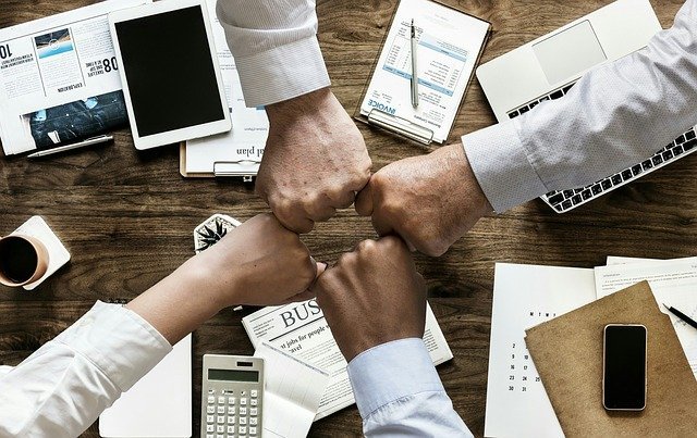 team who are growing during a recession putting their fists together over a work table