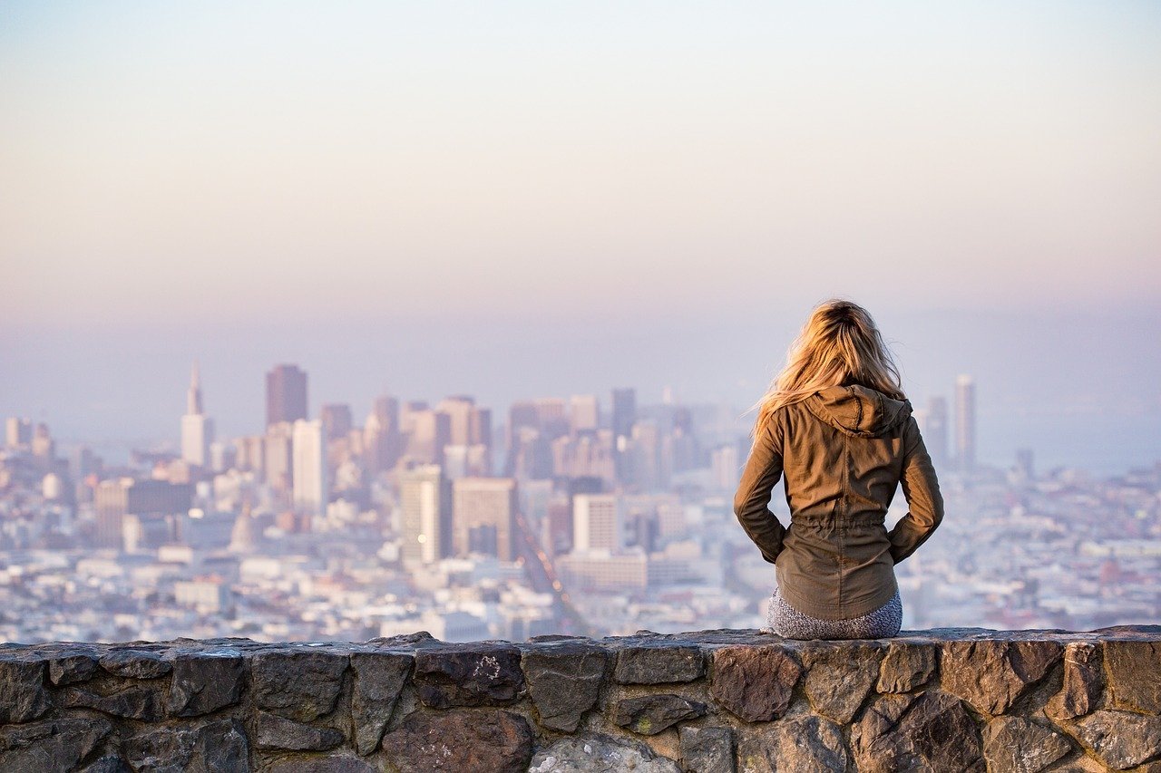 woman who likes travel sits on a low wall and watches city skyline