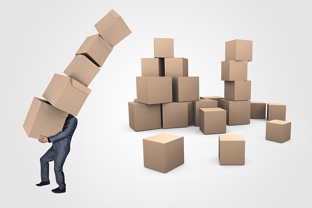 man in business suit who is gambling and not investing struggles with a tall pile of brown boxes