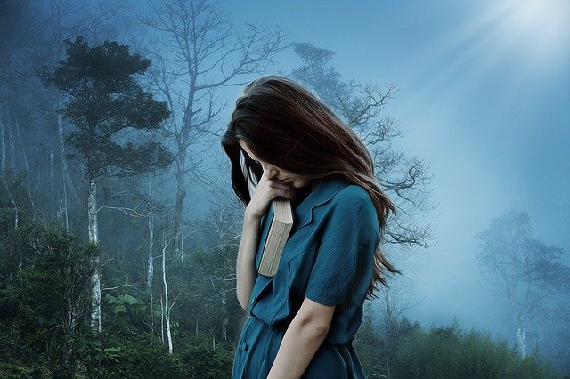 woman with leather-bound book in hand standing in dark forest with blue sky and trees in background