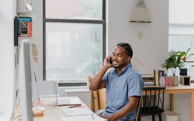 Effective communicator sitting at desk in office, talking on phone