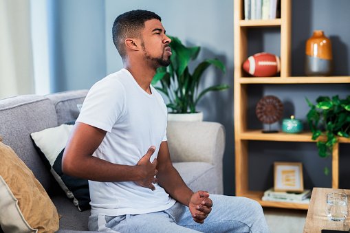 young man with prostate cancer clutching stomach while sitting on couch at home