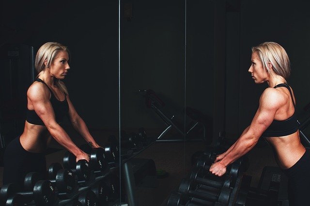 woman harnessing the power of difficult times by training with weights in a gym in front of mirror