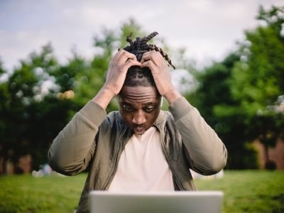 Black male entrepreneur with a laptop in a park stressed out while trying to make athe right decisions