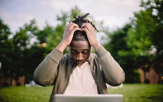 Black male entrepreneur with a laptop in a park stressed out while trying to make athe right decisions