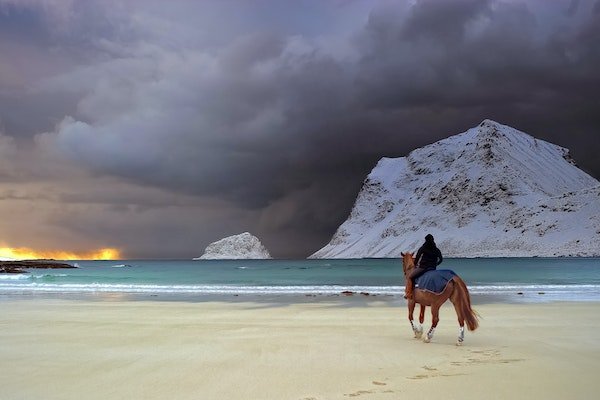 man in leadership position horseriding on beach with dark skies