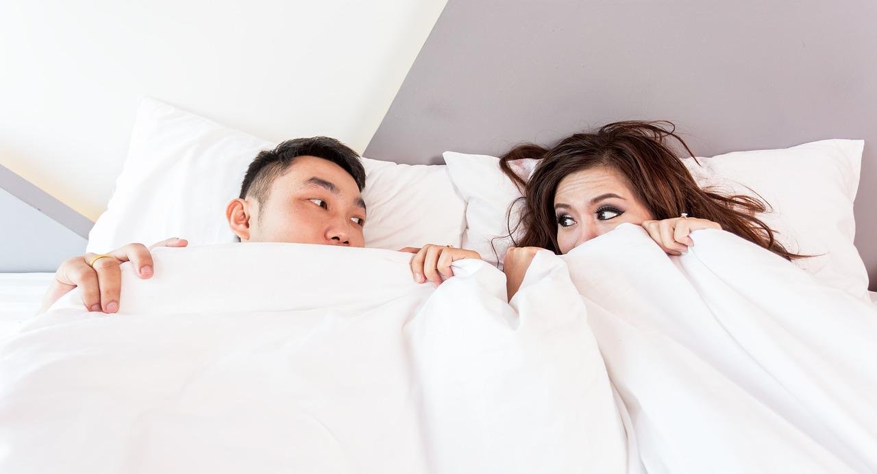 chinese man who has made his wife happy lying in bed with her under pure white sheets peeping out at each other