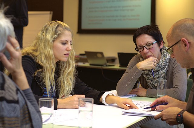 blond woman sitting with her co-workers at work table telling a co-worker that he screwed up