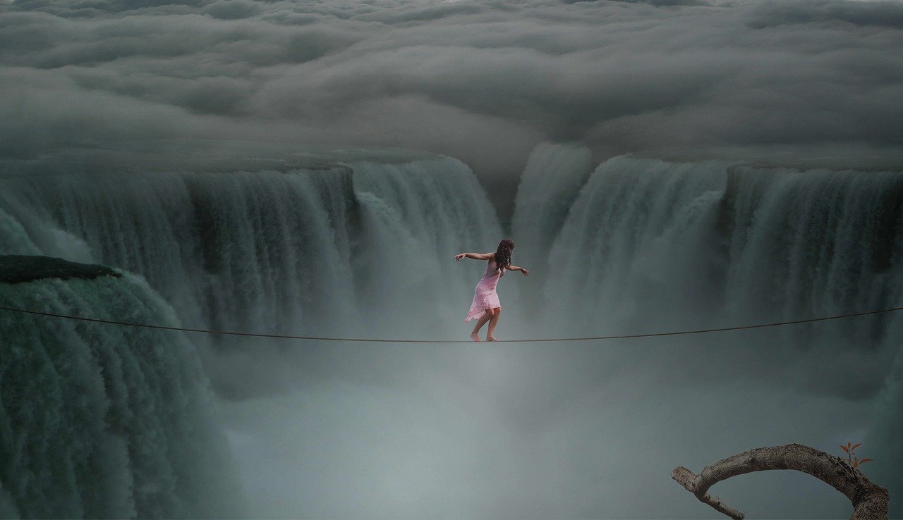 woman improving herself by walking on thin rope across a cliff with waterfall