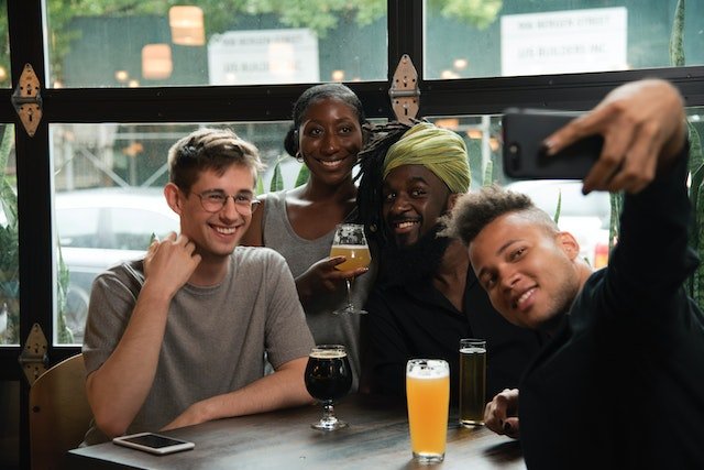 three men and one woman taking selfies in a cafe and enjoying the weekend
