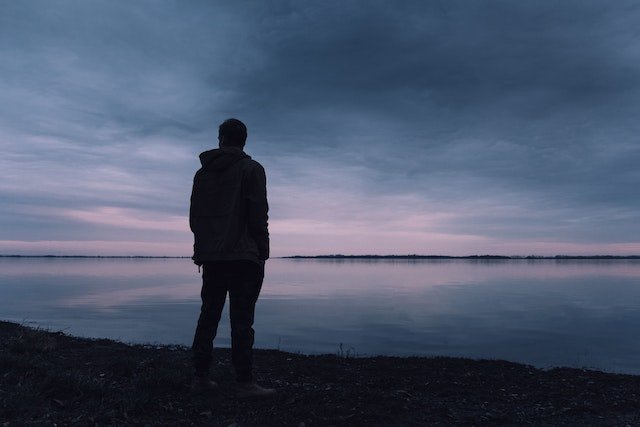 man reflecting on his life beside a lake at night