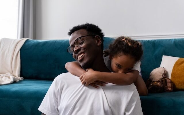 young african father in white shirt playing with his daugter on blue couch in sitting room at daytime